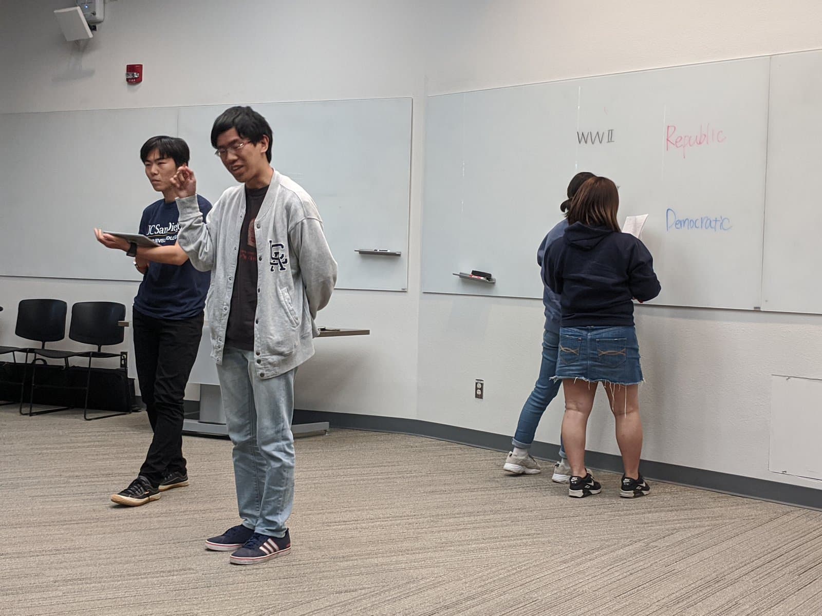 教室のホワイトボードの前で発表する参加学生。ボードには英語で講義のキーワードが書かれています。